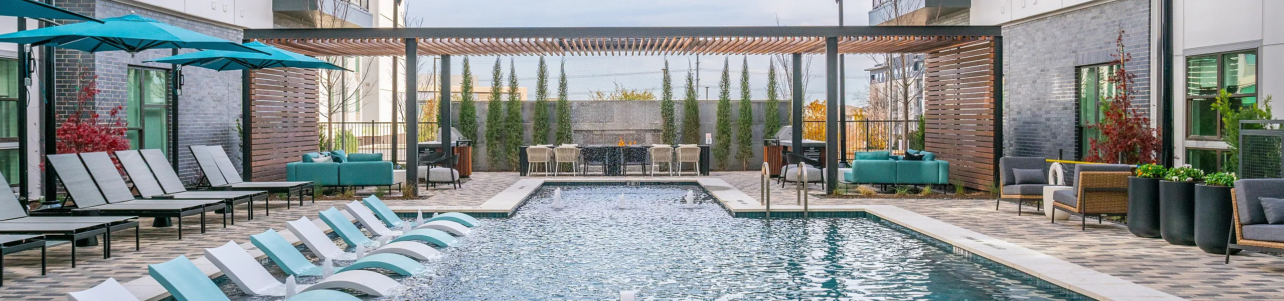 Modern apartment complex featuring a luxurious outdoor swimming pool with sun loungers, stylish seating areas, and chic pergola accents.