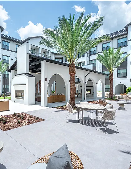 Luxurious apartment complex courtyard featuring contemporary outdoor seating, tropical palm trees, and a modern fireplace under a bright blue sky.
