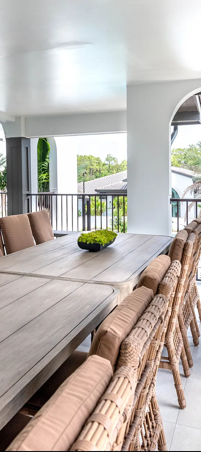 Inviting covered patio dining area with a long wooden table, padded chairs, and lush greenery, perfect for entertaining with a view.