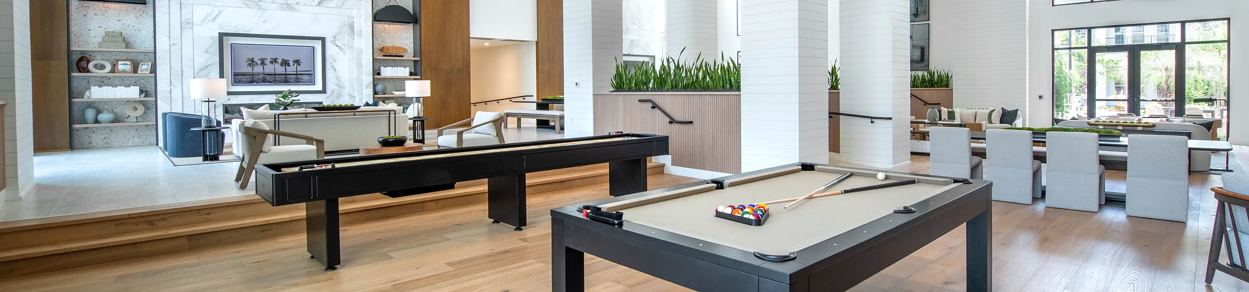 Bright and spacious recreational area featuring modern pool tables, elegant seating, and floor-to-ceiling windows for natural light.