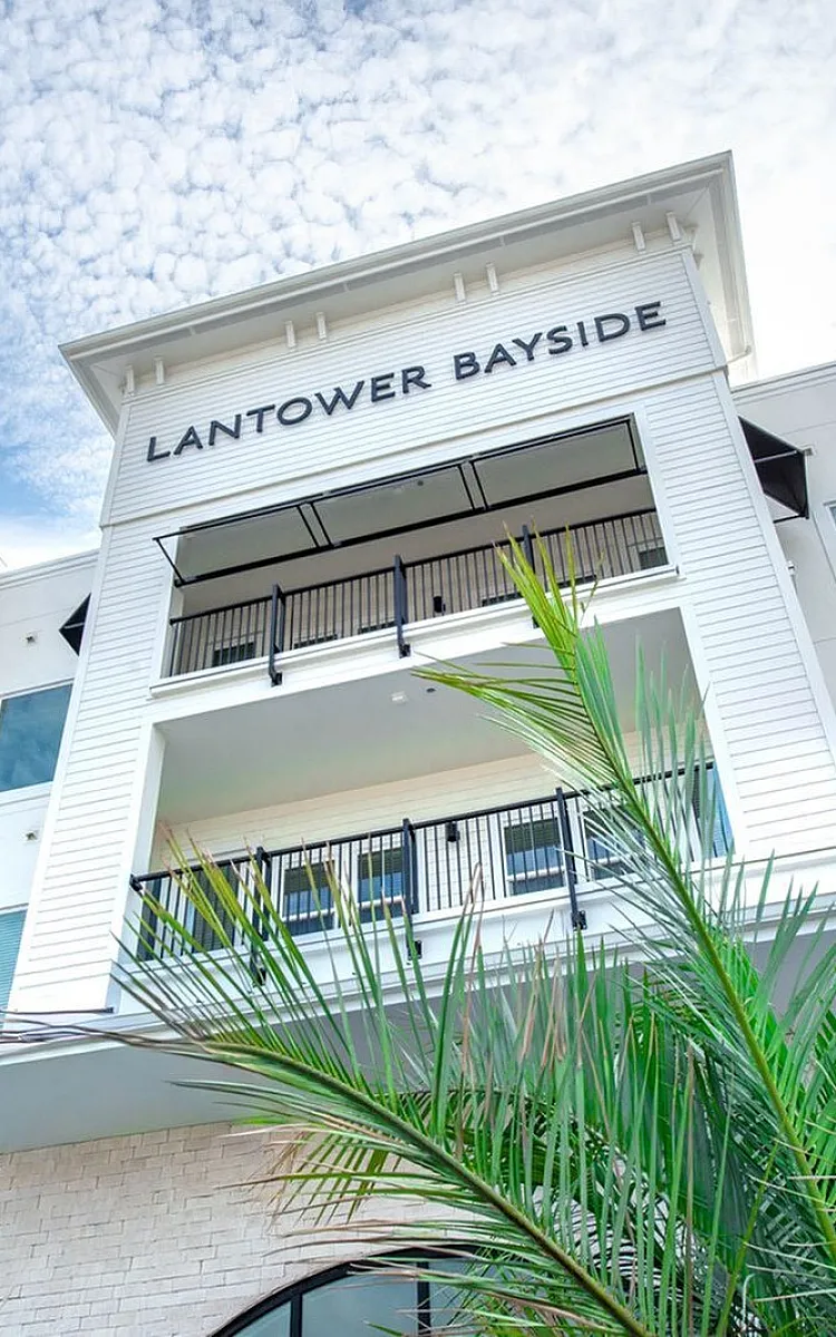 Modern apartment exterior at Lantower Bayside, featuring elegant balconies, lush greenery, and a bright, welcoming facade against a picturesque sky.