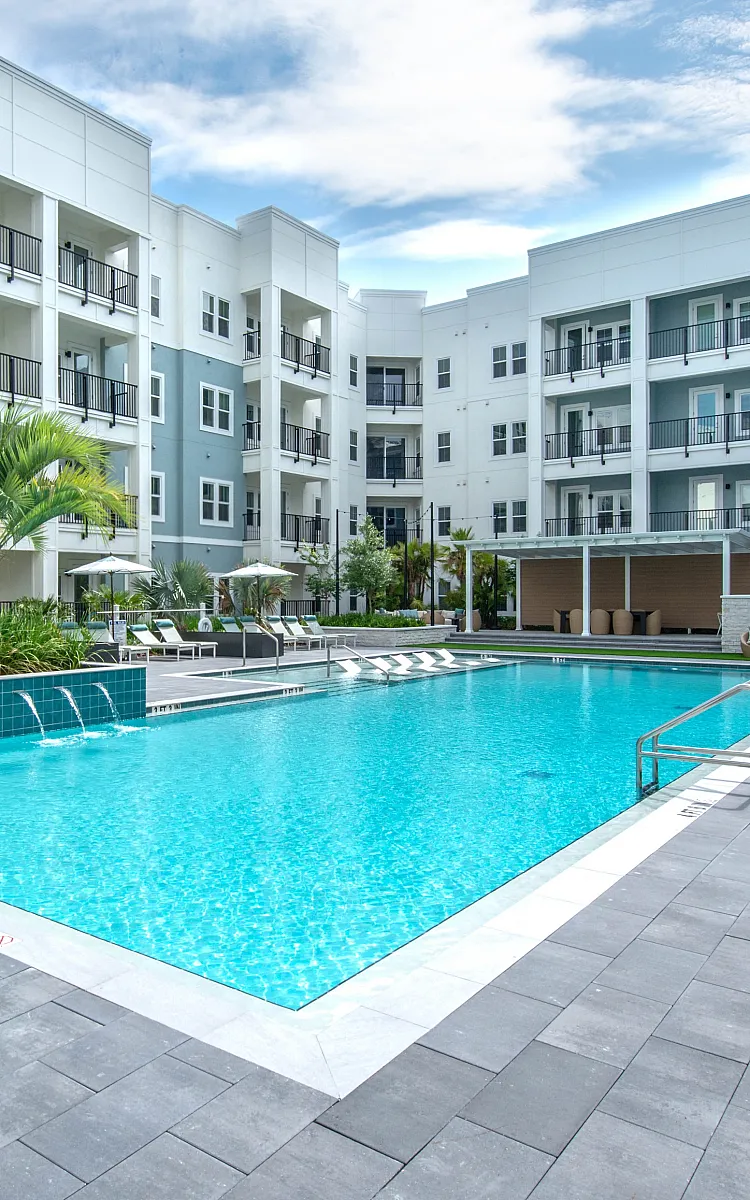 Luxurious apartment complex with a sparkling outdoor pool, surrounded by modern balconies and lush greenery.