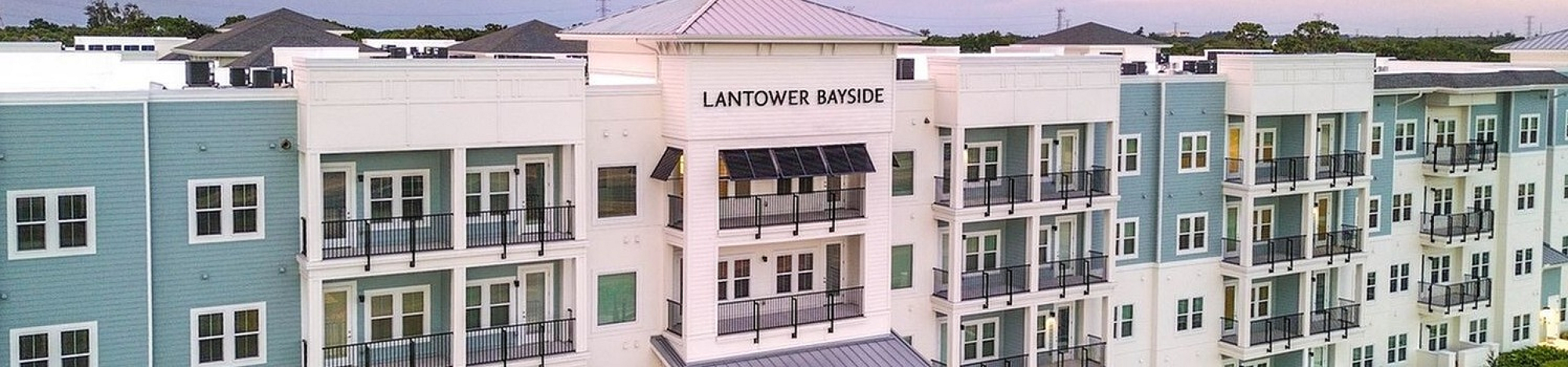 Elegant Lantower Bayside apartment complex at sunset, showcasing modern balconies, lush landscaping, and ample parking.