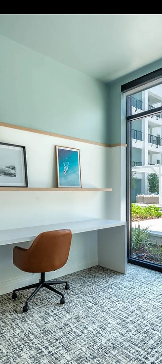 Bright study space with modern desk and art, overlooking a lush courtyard in a contemporary apartment complex.