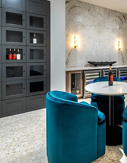 Elegant lounge area with vibrant teal chairs, chic marble tables, and a sophisticated wall wine rack, creating a luxurious ambiance.