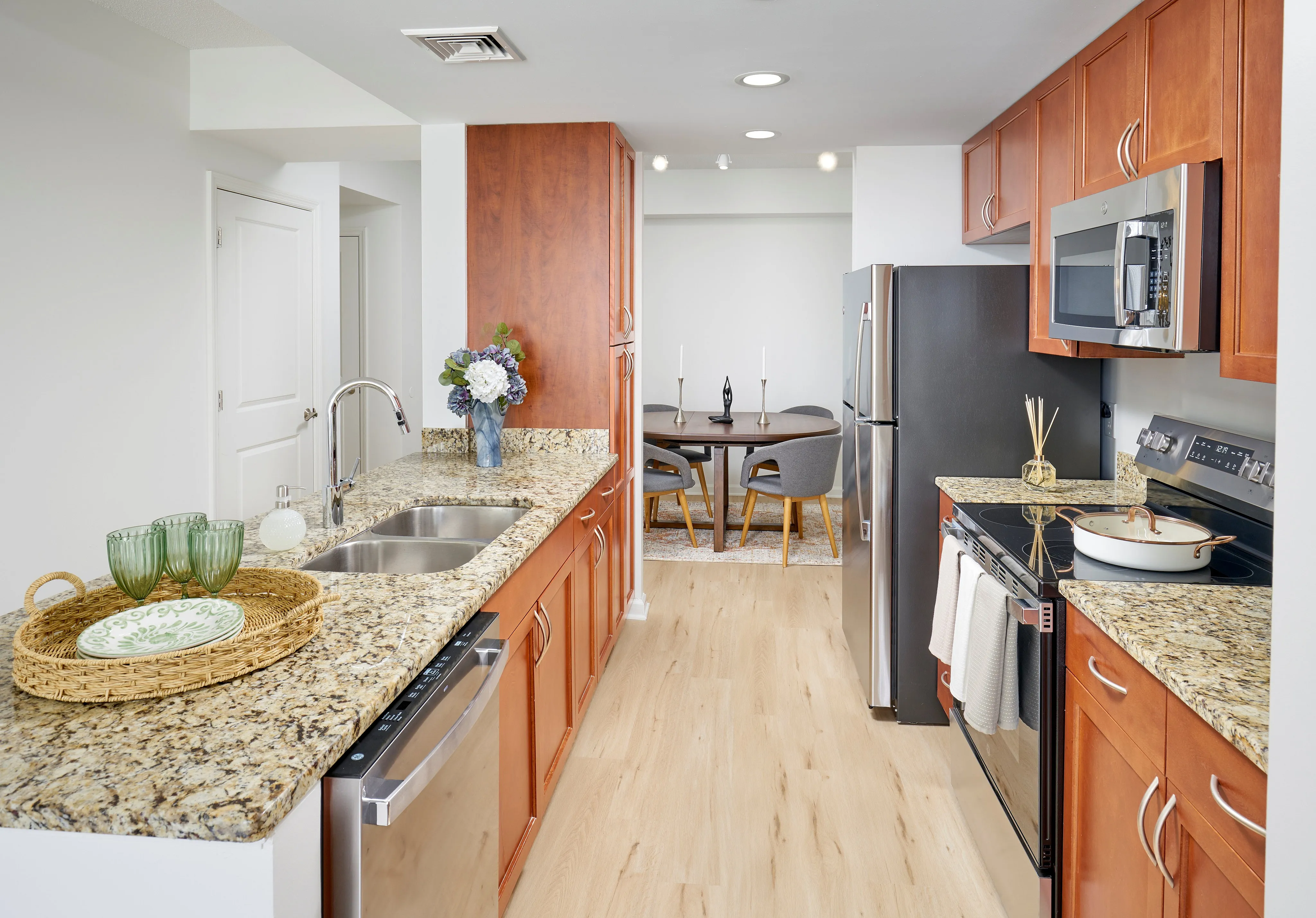 Newly renovated Ellington One Bedroom kitchen at Meridian at Grosvenor Station featuring sleek stainless steel appliances, modern vinyl plank wood-style flooring, and updated lighting fixtures that complement existing granite countertops and custom cabinetry | Newly Renovated Kitchen | Meridian at Grosvenor Station | North Bethesda MD Apartments | Rockville MD Apartments