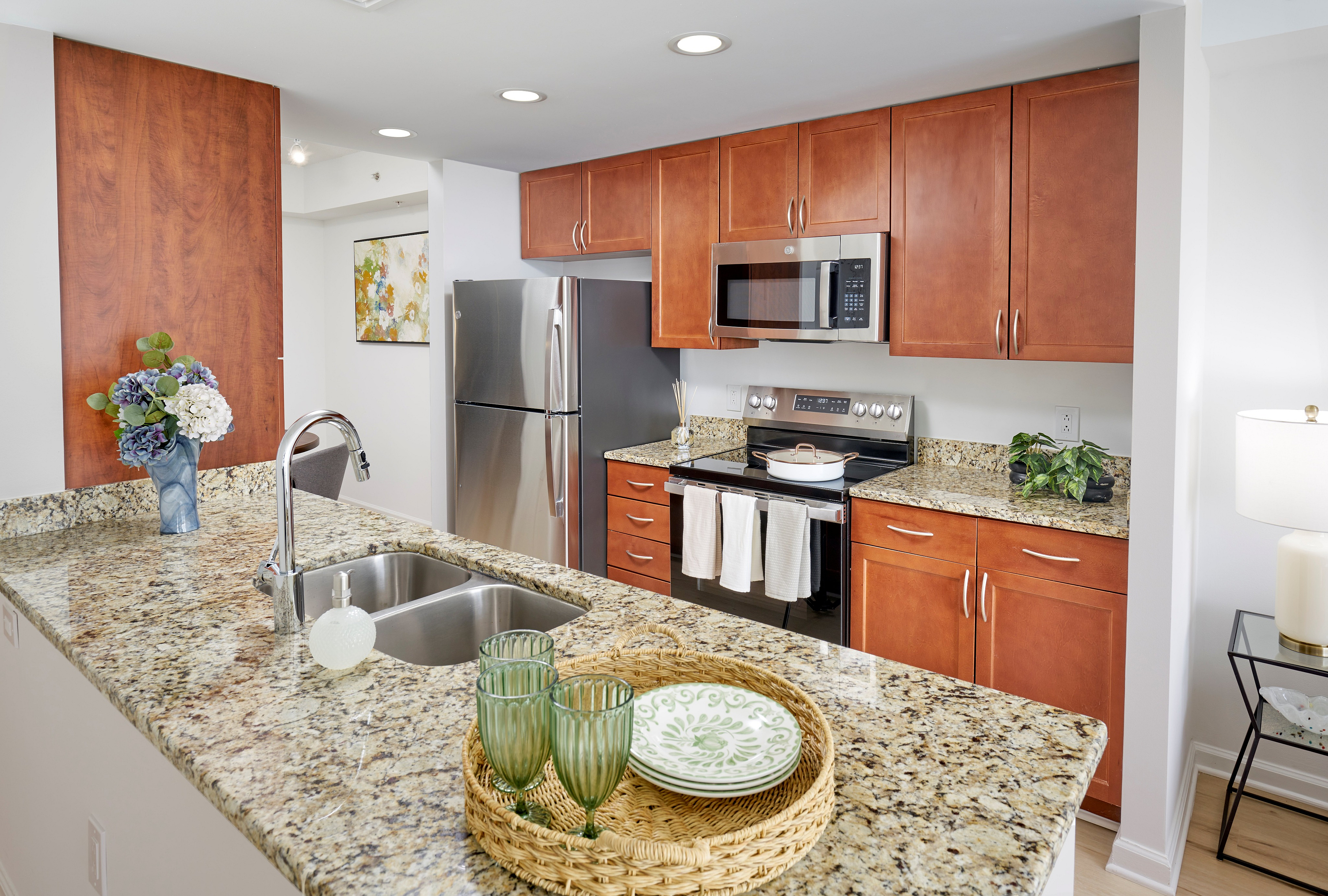 Newly renovated kitchen at Meridian at Grosvenor Station featuring sleek stainless steel appliances, modern vinyl plank wood-style flooring, and updated lighting fixtures that complement existing granite countertops and custom cabinetry | Newly Renovated Kitchen | Meridian at Grosvenor Station | North Bethesda MD Apartments | Rockville MD Apartments