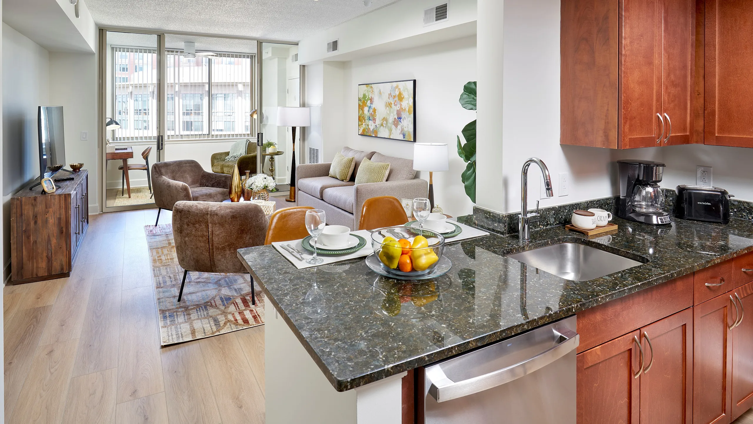 Renovated Newport one bedroom floor plan apartment kitchen at Meridian at Eisenhower Station with granite countertops, stainless steel appliances, and living area with wood-style flooring. | Luxury Alexandria VA Apartments | Meridian at Eis