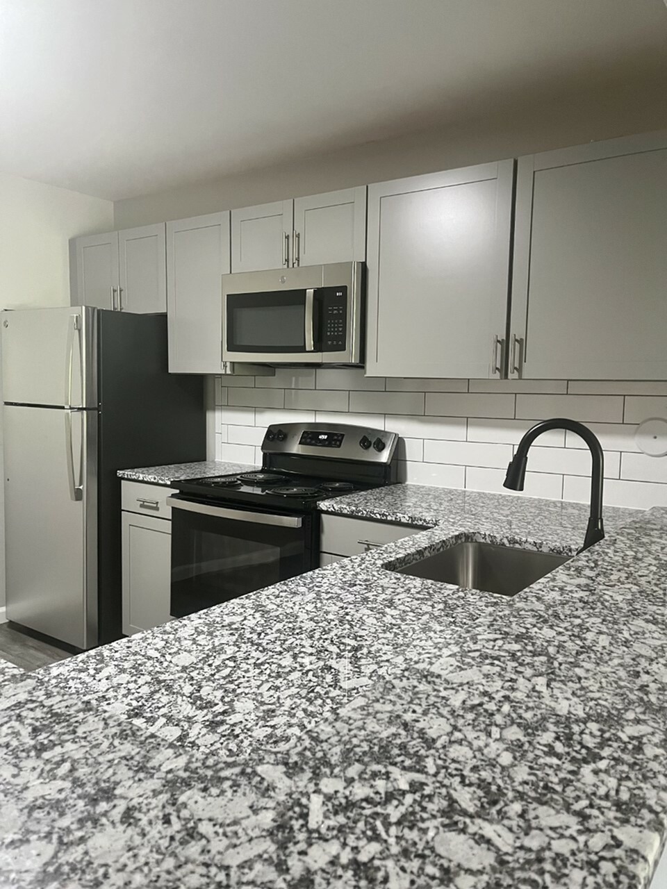 Kitchen has soft grey cabinets with a grey, black, white granite counter tops