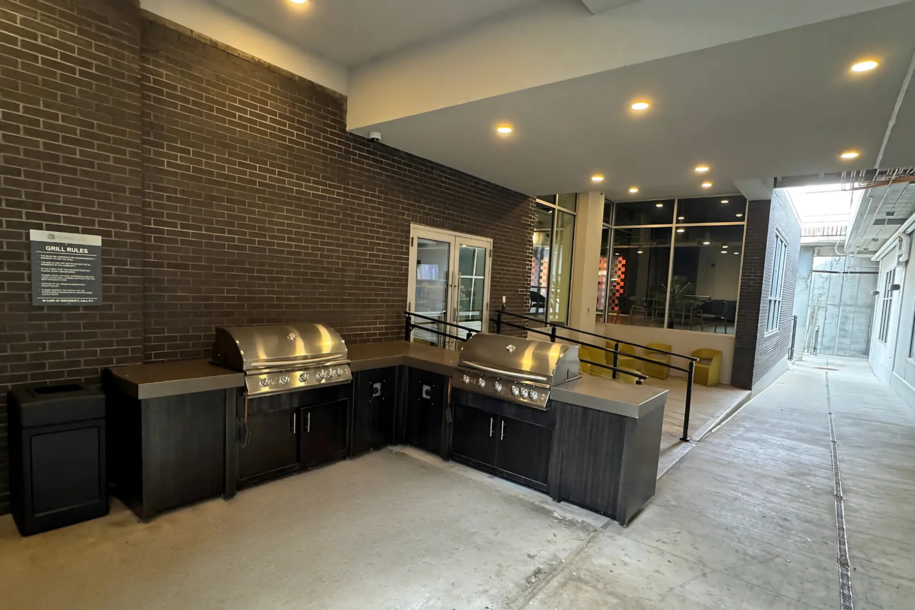 Modern outdoor grilling station with sleek stainless steel grills set against a stylish brick wall, illuminated by ambient lighting.