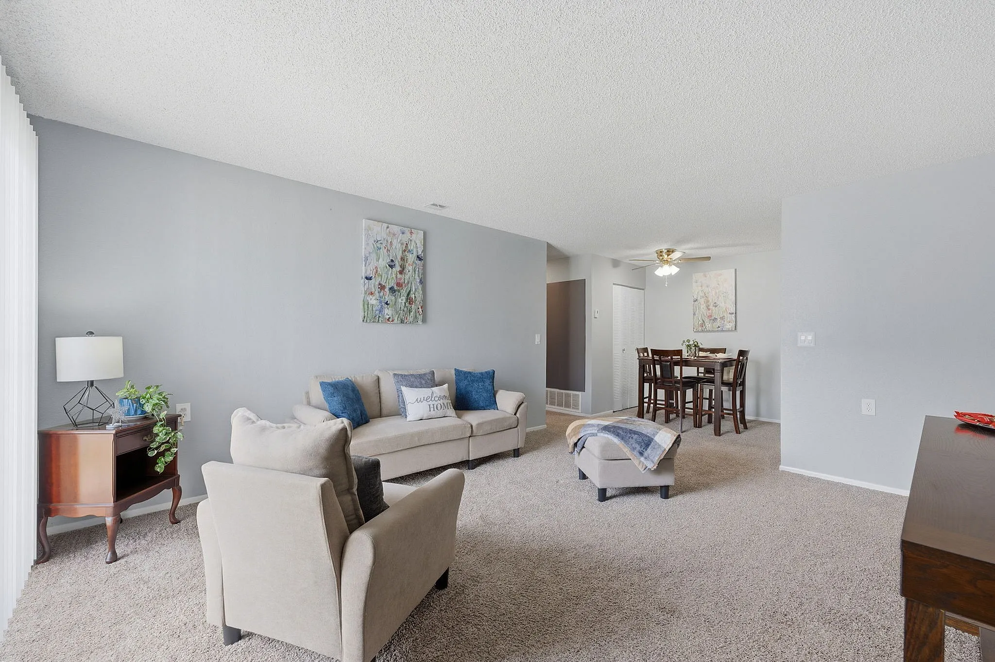 Inviting open-plan living and dining area with cozy furnishings, accented by soft carpeting and elegant wall art.