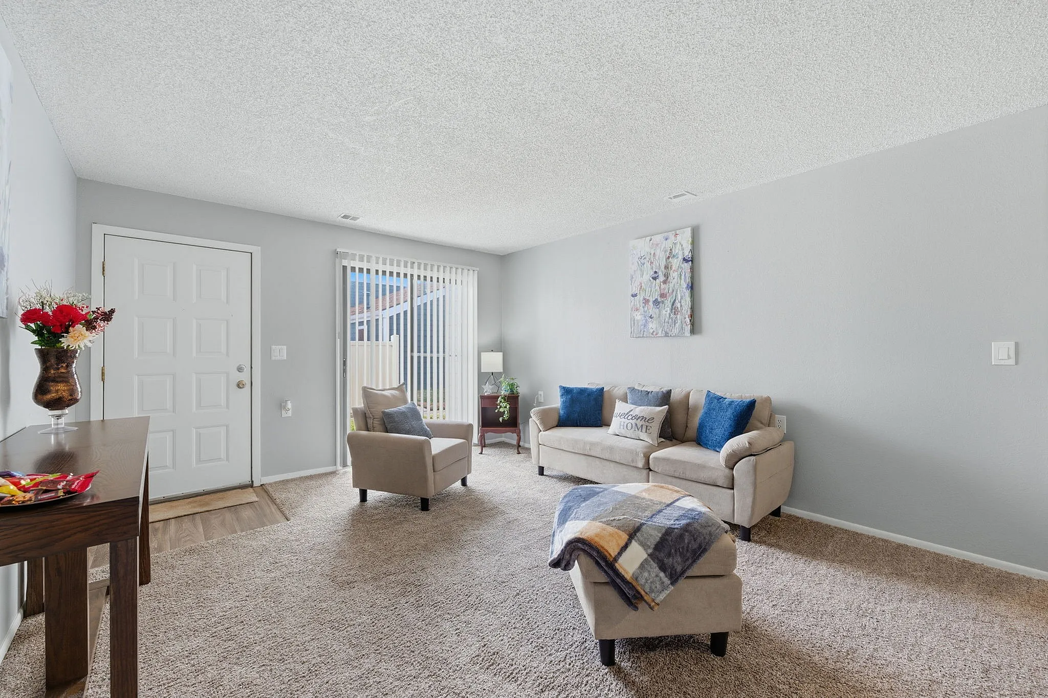 Inviting living room with cozy beige furniture, vibrant cushion accents, and abundant natural light through large sliding doors.