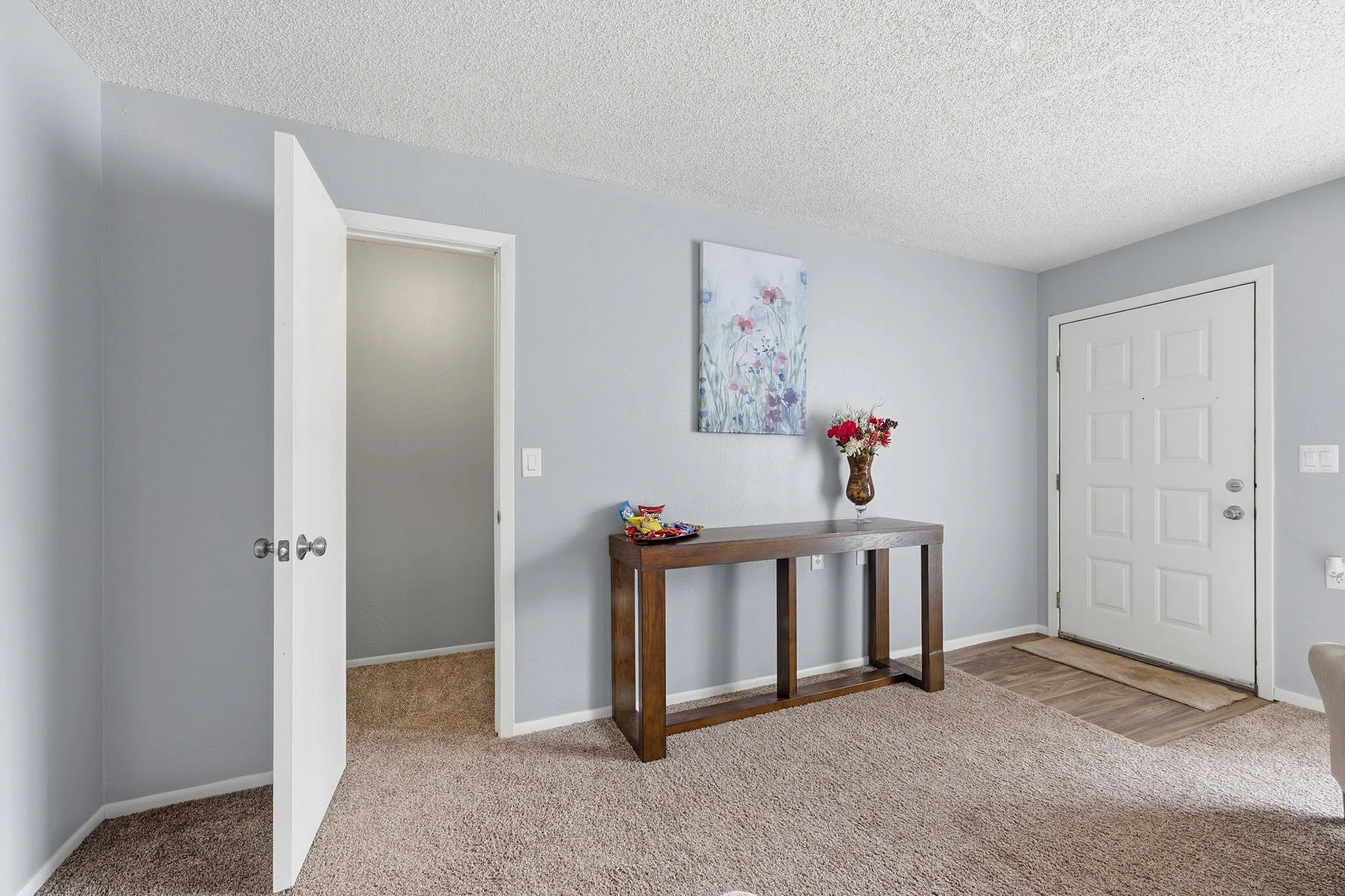 Inviting entryway featuring an elegant wooden console table with decorative flowers, neutral-toned walls, and plush carpeting.