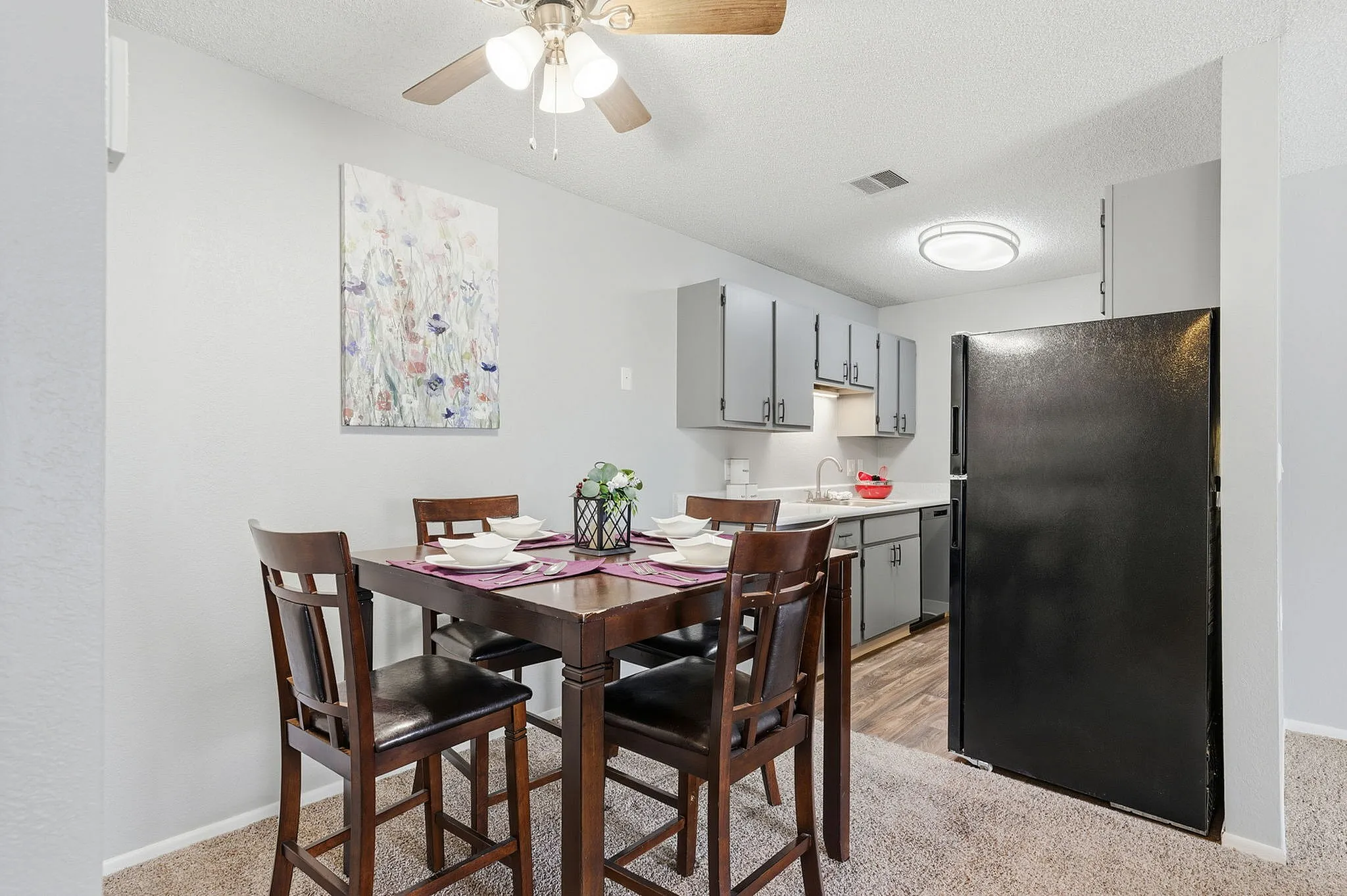 Modern dining area with elegant setup featuring a stylish wooden table, four cushioned chairs, chic gray cabinets, and a sleek black refrigerator.