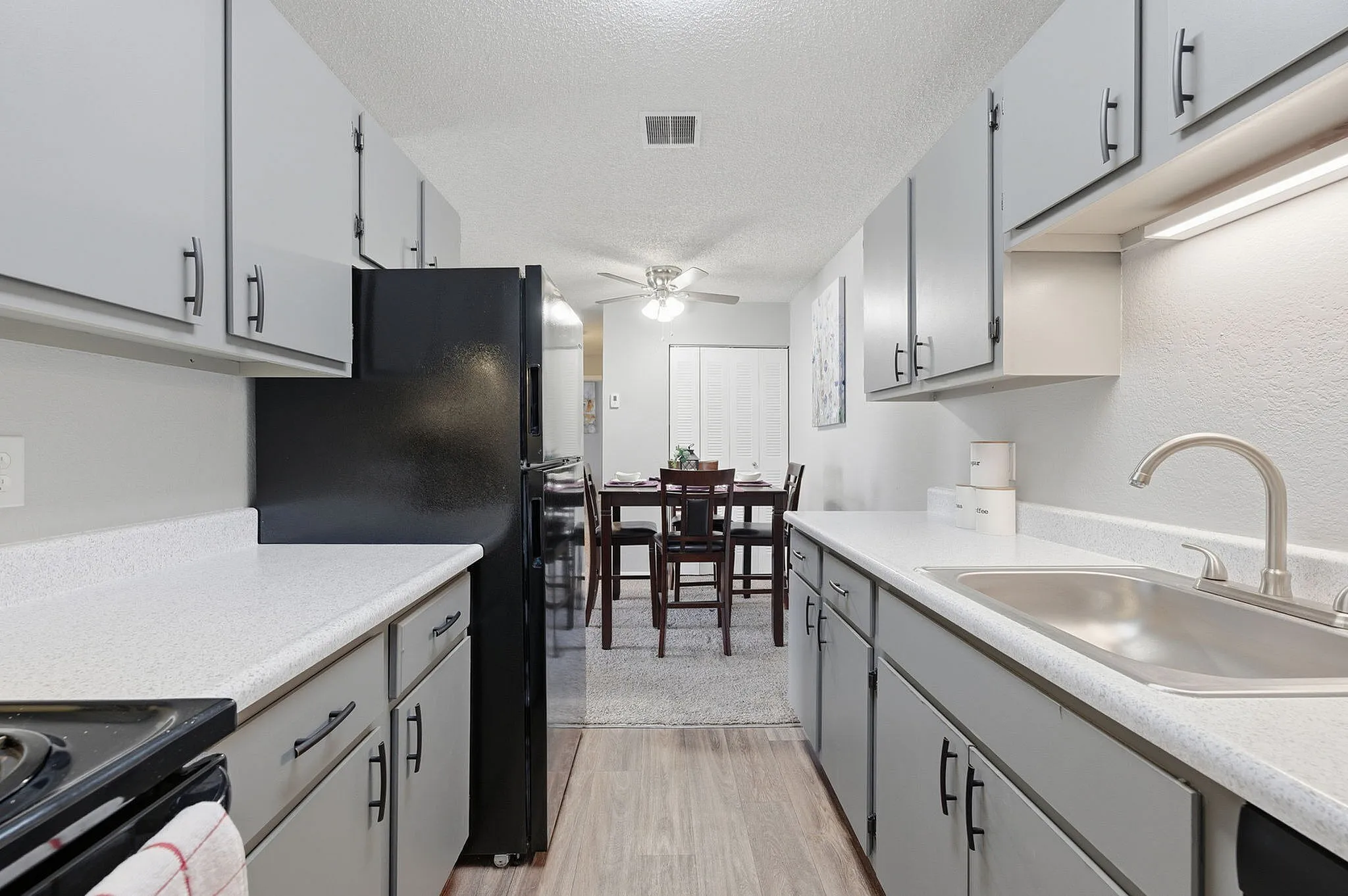 Modern kitchen with sleek gray cabinets, stainless steel sink, and spacious countertops leading to a cozy dining area.