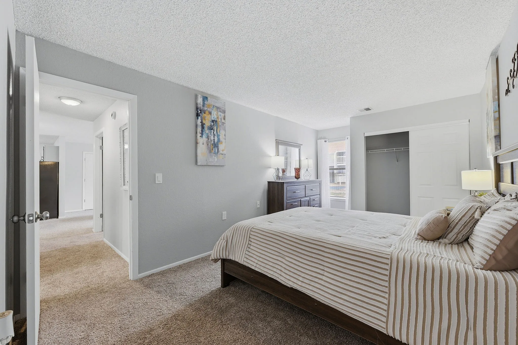 Inviting bedroom with elegant decor, featuring a plush bed, stylish art pieces, and ample natural light from large windows.