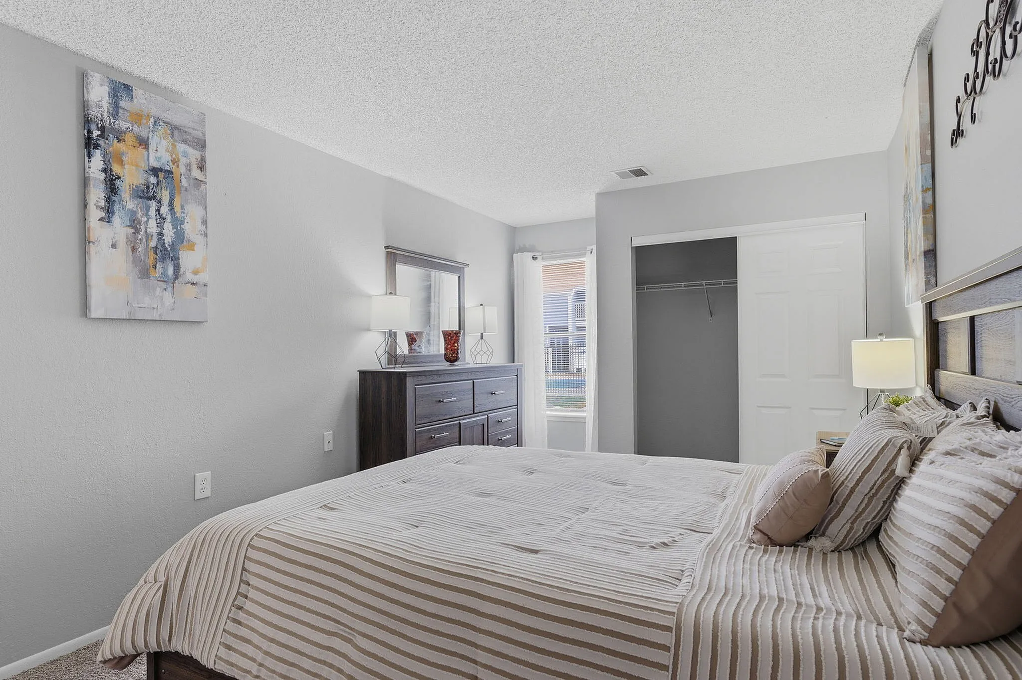 Inviting bedroom with modern decor, featuring plush bedding, stylish artwork, and ample natural light from a large window.