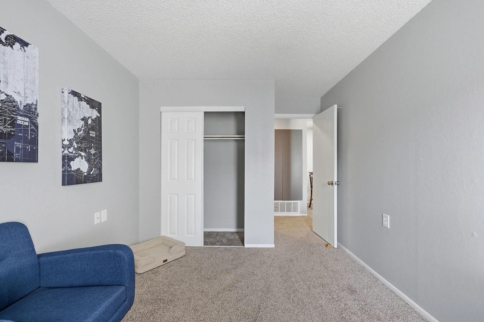 Inviting bedroom with a soft carpet, modern gray walls, and chic wall art, featuring an open closet and a cozy blue chair.