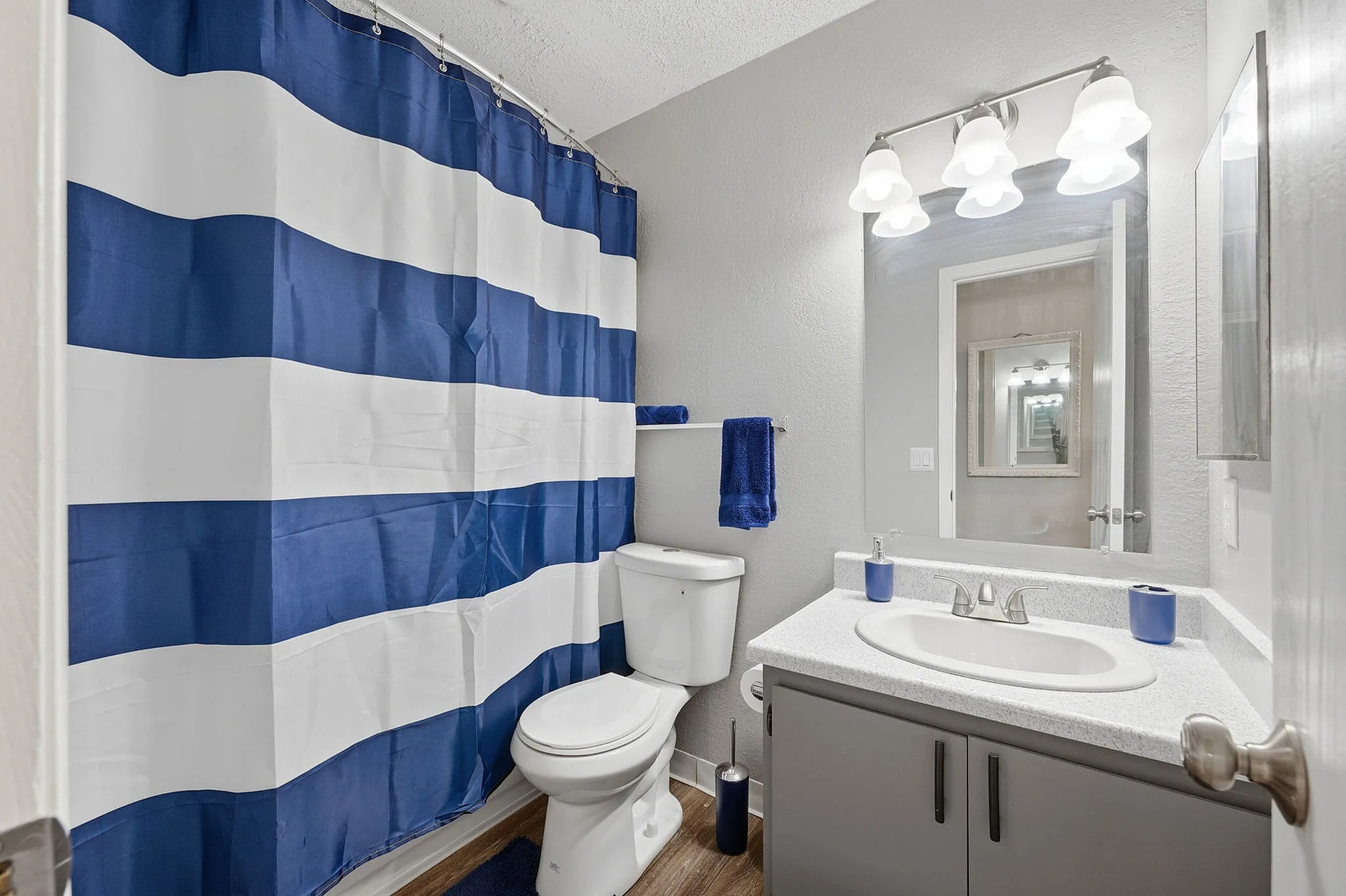 Bright and modern bathroom featuring a sleek vanity, elegant lighting, and bold blue-striped shower curtain.