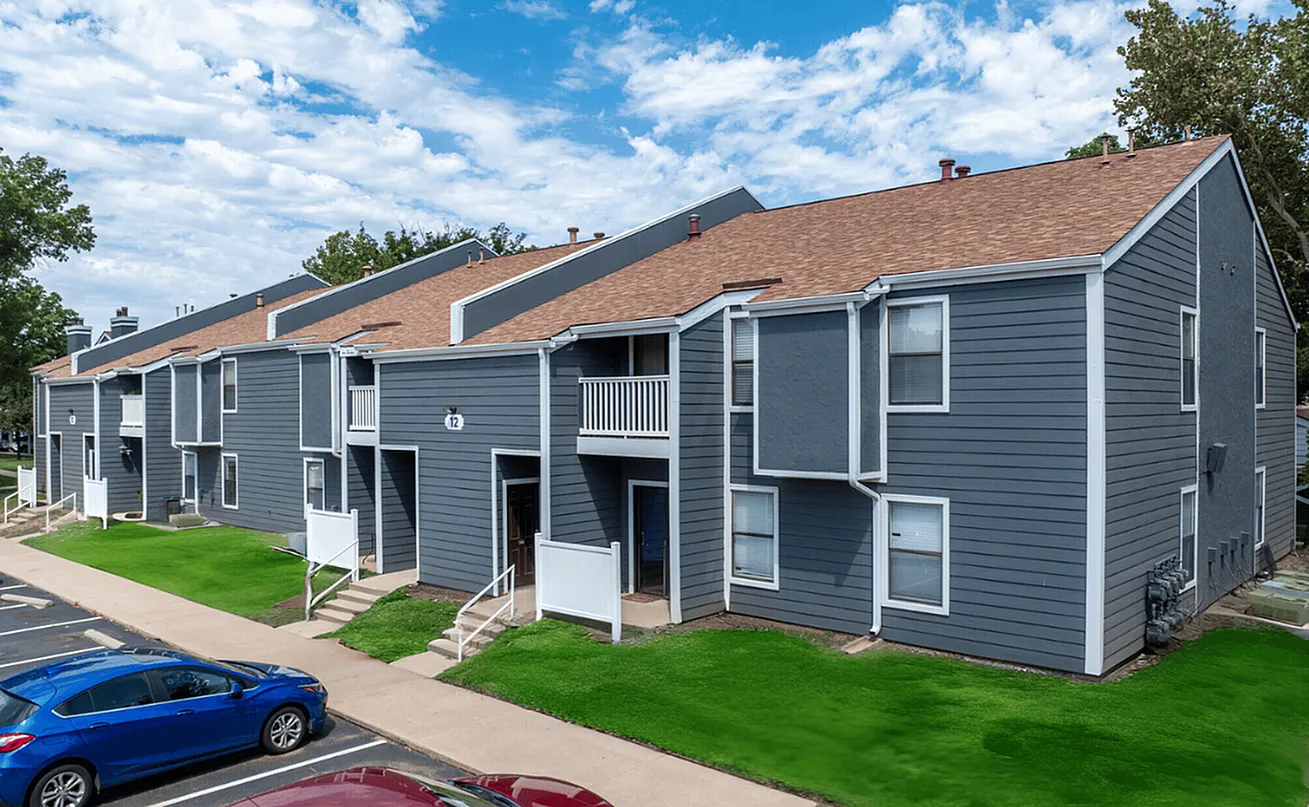 Modern apartment complex with sleek gray exterior and lush green lawns under a vibrant blue sky.