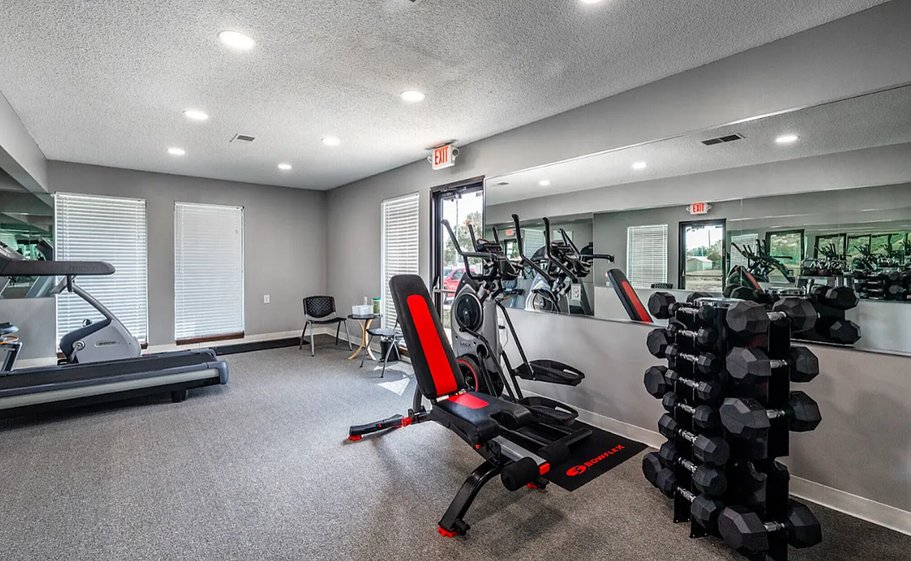 Modern fitness center with state-of-the-art equipment, including treadmills, strength machines, and a set of dumbbells, set in a bright, spacious room with ample natural light.