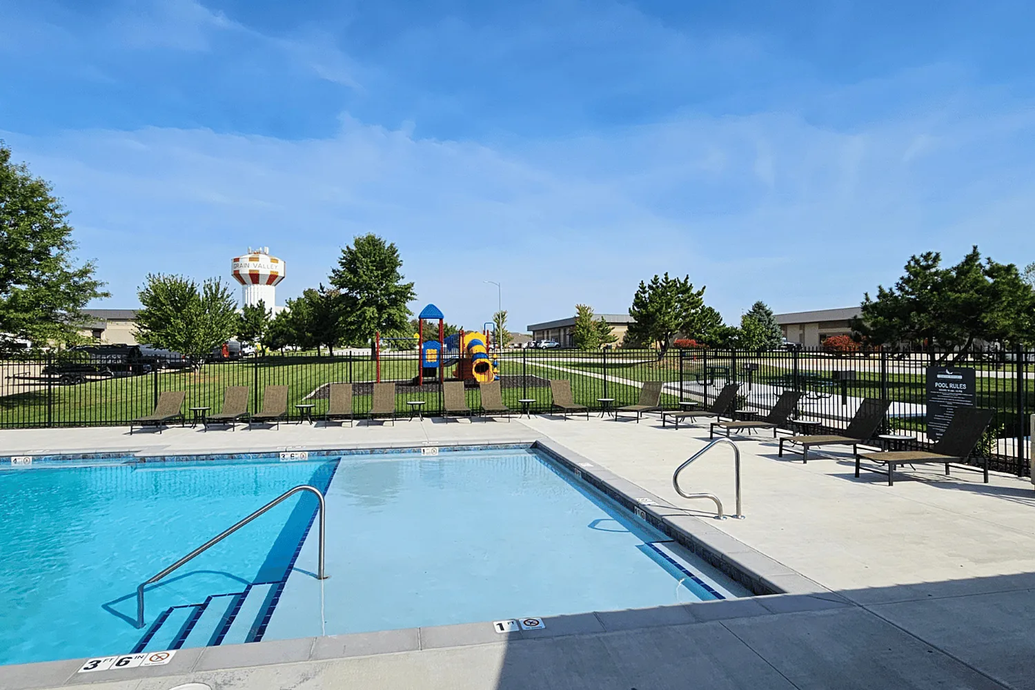 Vibrant outdoor pool area with inviting lounge chairs, a colorful playground, and lush green spaces, perfect for leisure and family fun.