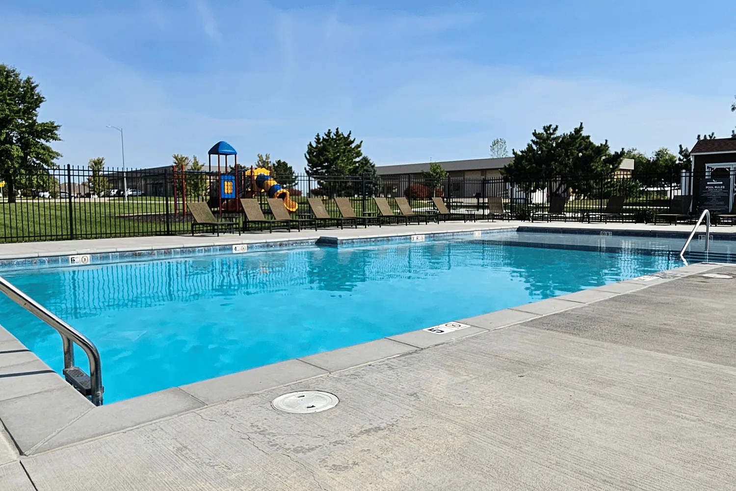 Inviting outdoor pool area with lounge chairs and a vibrant playground, perfect for family relaxation and fun.