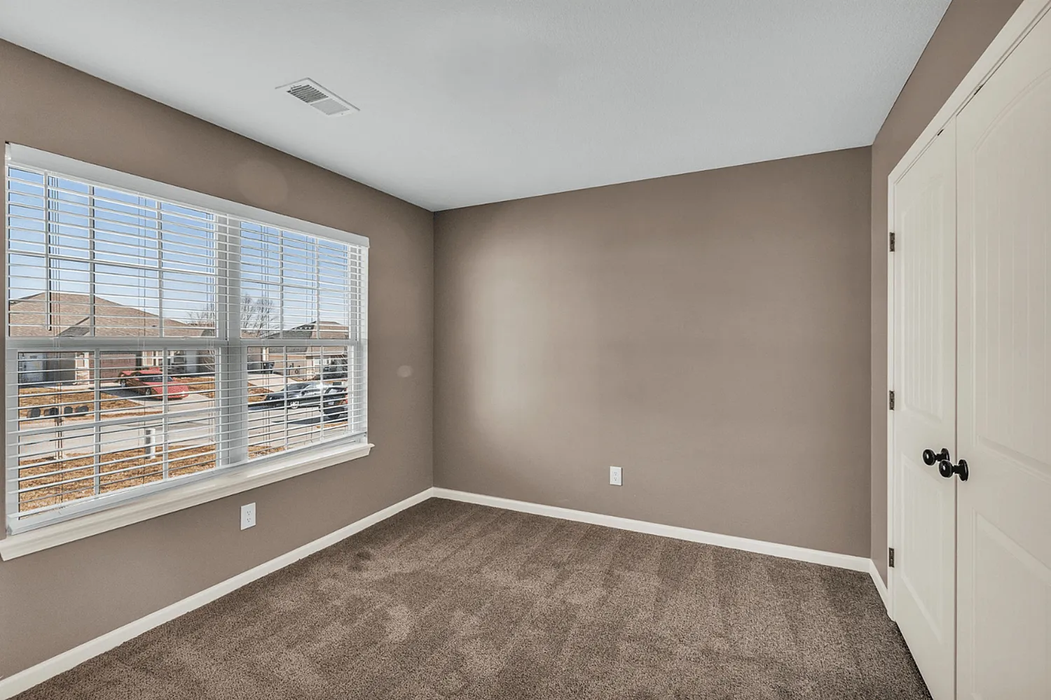 Bright and cozy room with large windows, plush carpet, and neutral walls, ideal for creating a personalized space.
