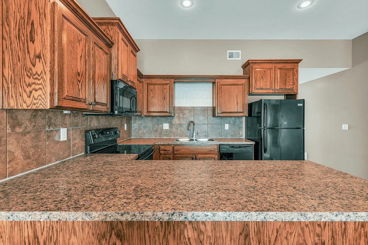 Charming kitchen with elegant wooden cabinetry, modern black appliances, and a sleek granite countertop.