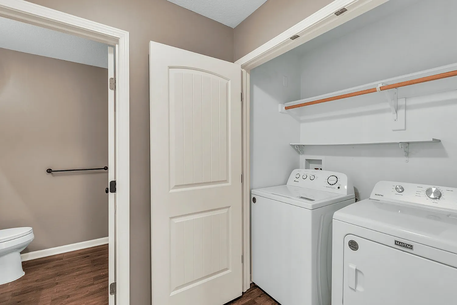 Modern laundry area with washing machine and dryer in a sleek apartment, featuring wood flooring and ample shelving.