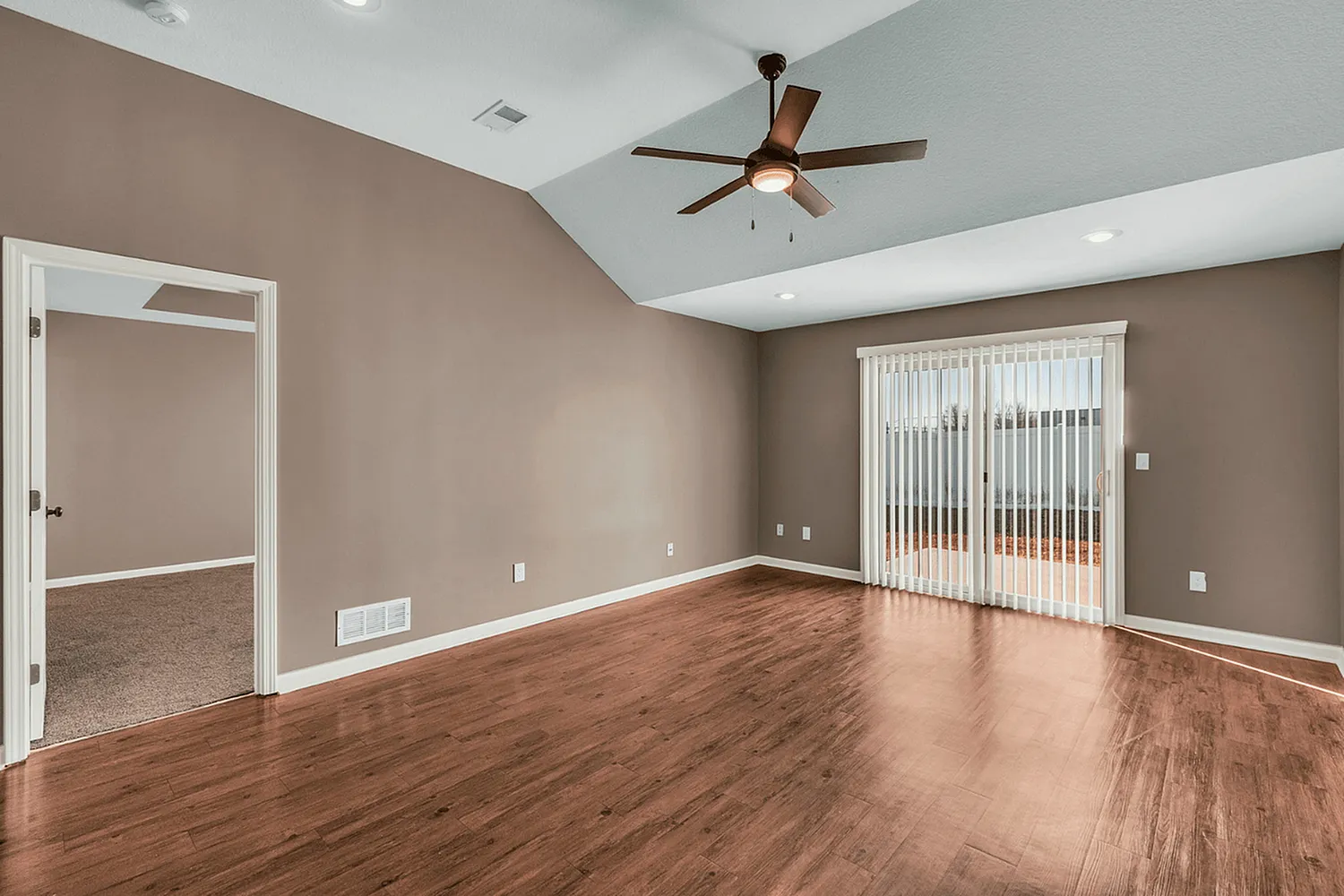 Inviting living space featuring elegant hardwood floors, a modern ceiling fan, and abundant natural light from large sliding glass doors.