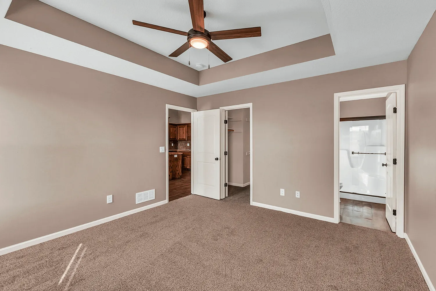 Inviting bedroom with plush carpet, stylish ceiling fan, and walk-in closet, seamlessly connected to kitchen and modern bathroom.