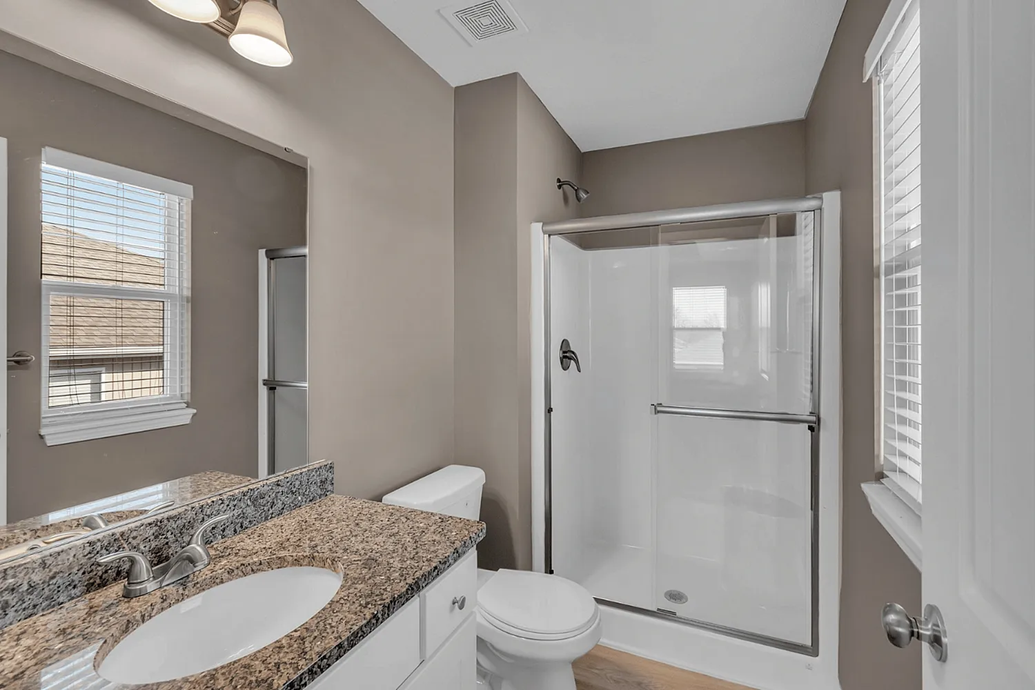 Sleek and modern bathroom with elegant granite countertop, glass-enclosed shower, and ample natural light.