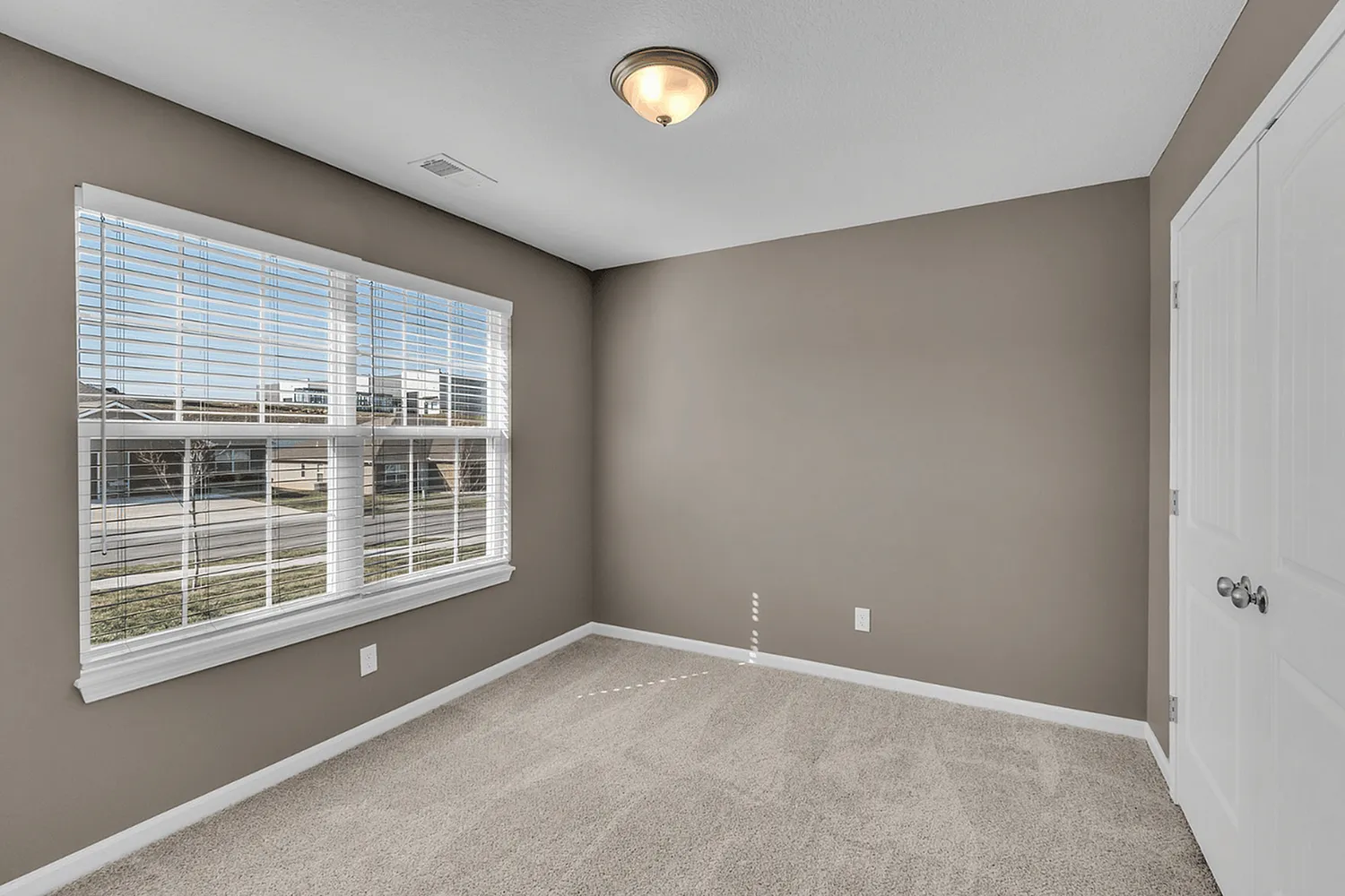 Bright and modern bedroom with plush carpet, large window, and elegant double doors, offering a tranquil atmosphere.