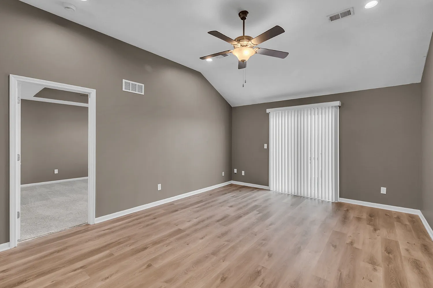 Bright and spacious living area with elegant hardwood flooring, featuring a ceiling fan and large sliding glass doors opening to natural light.