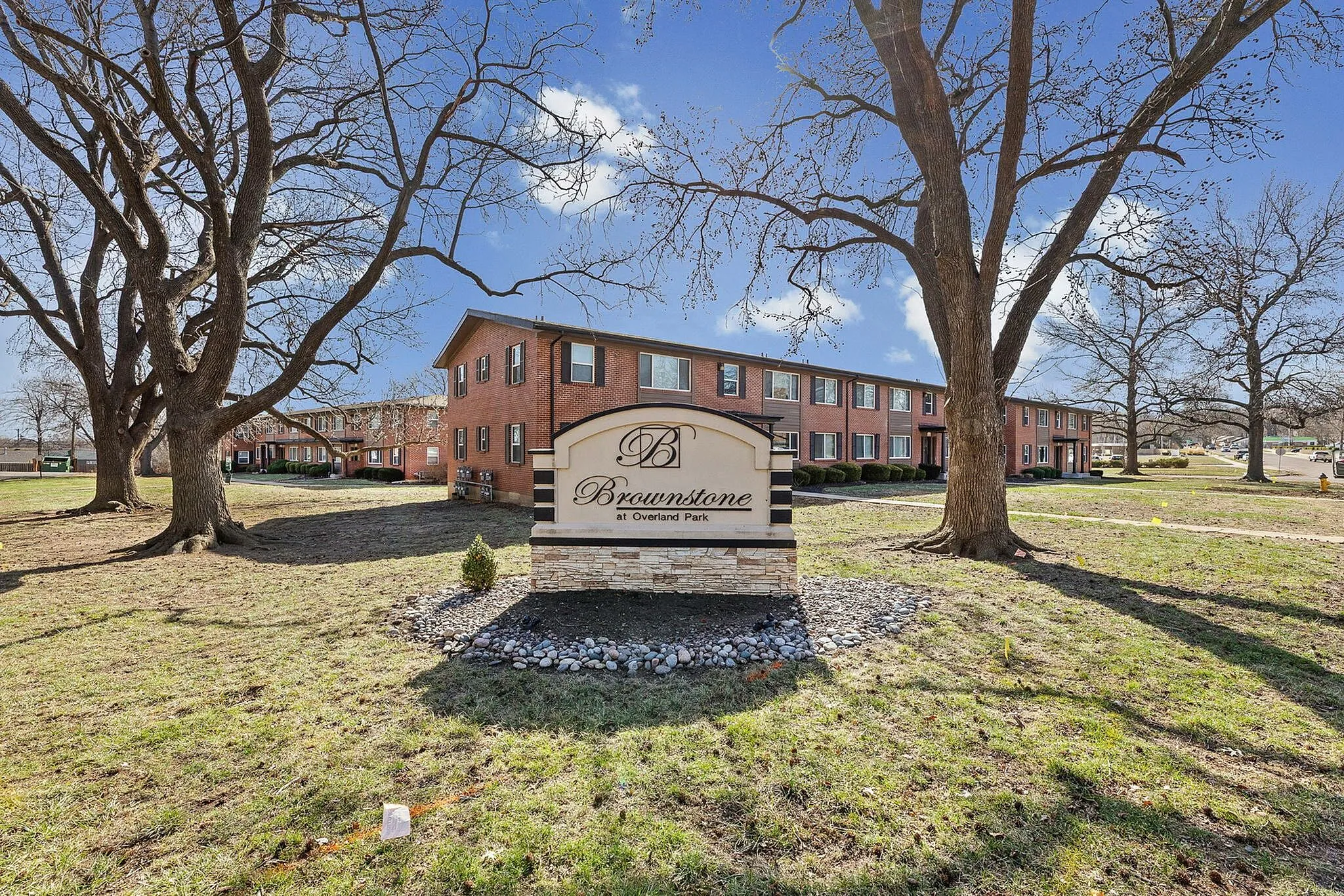 Inviting view of Brownstone at Overland Park, featuring classic brick apartments set amidst a spacious, tree-lined landscape.
