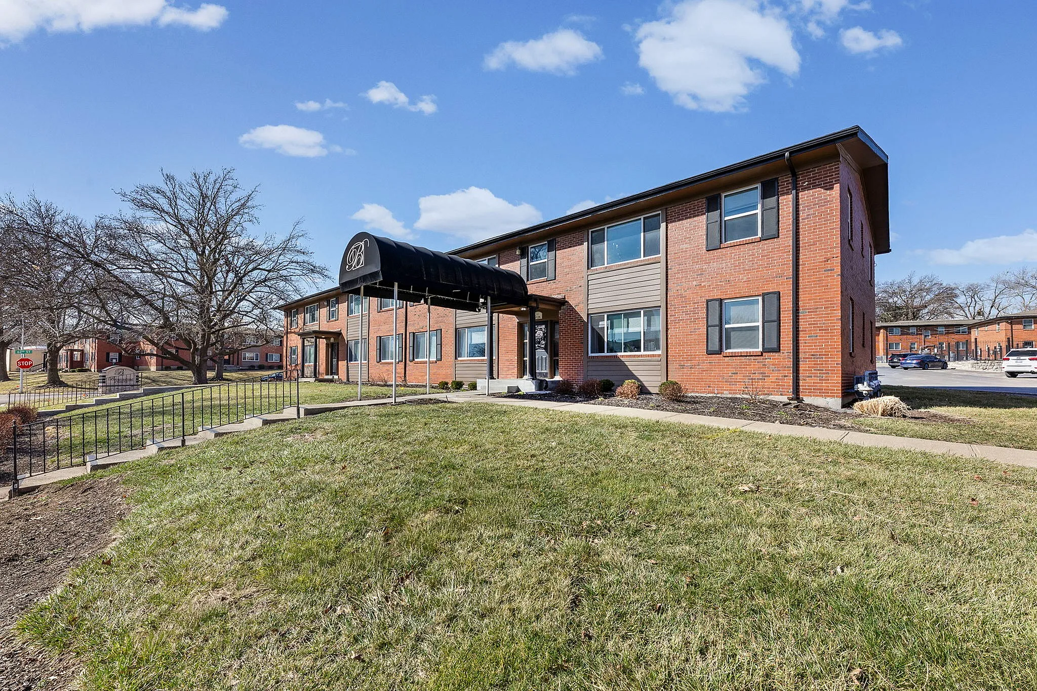 Inviting brick apartment building with stylish facade, manicured lawn, and a welcoming entrance under a charming canopy.