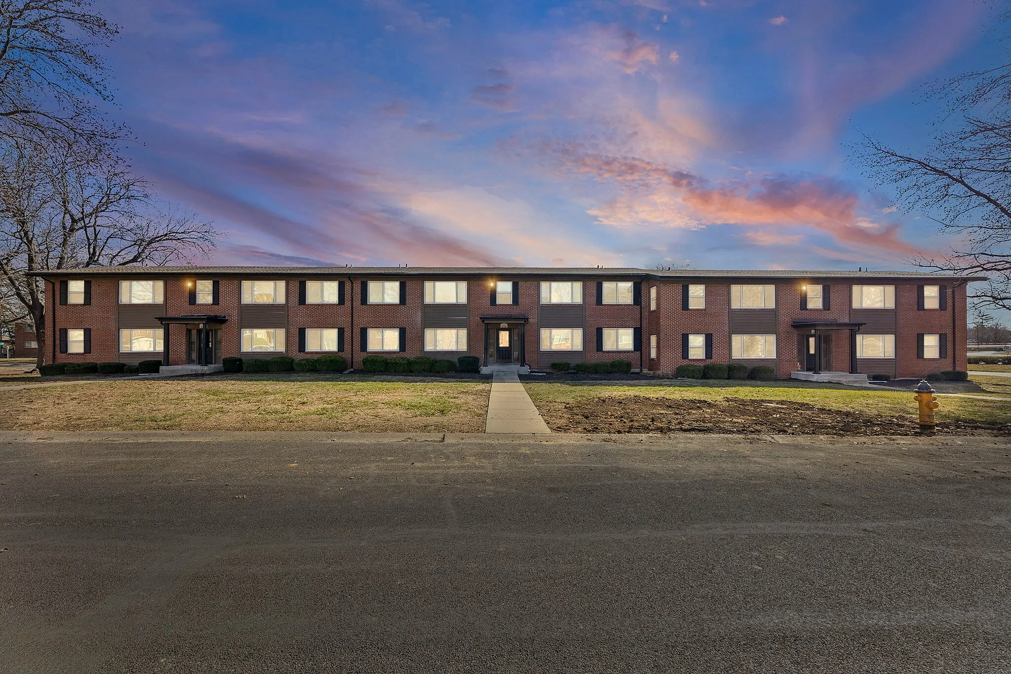 Charming red-brick apartment building under a vibrant sunset sky, offering a welcoming and serene neighborhood atmosphere.