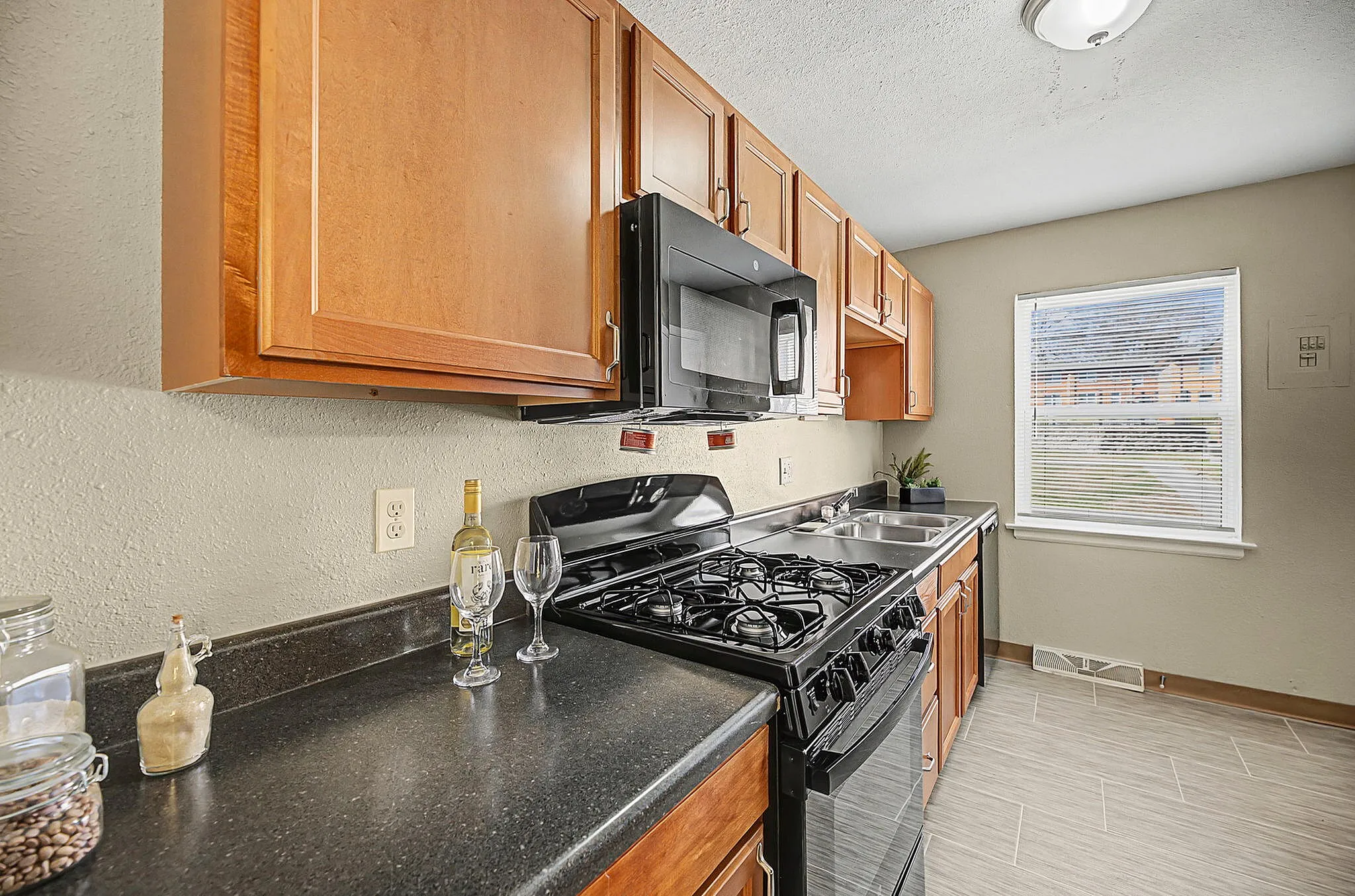 Charming kitchen with sleek black stove, microwave, and elegant wooden cabinets, featuring a sunny window and cozy atmosphere.