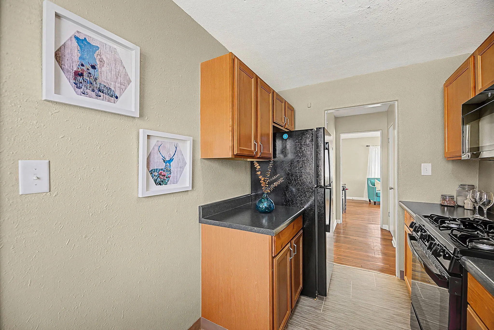 Charming kitchen with warm wooden cabinets, sleek black countertops, and modern appliances, highlighted by artistic wall decor and a touch of greenery in a stylish vase.