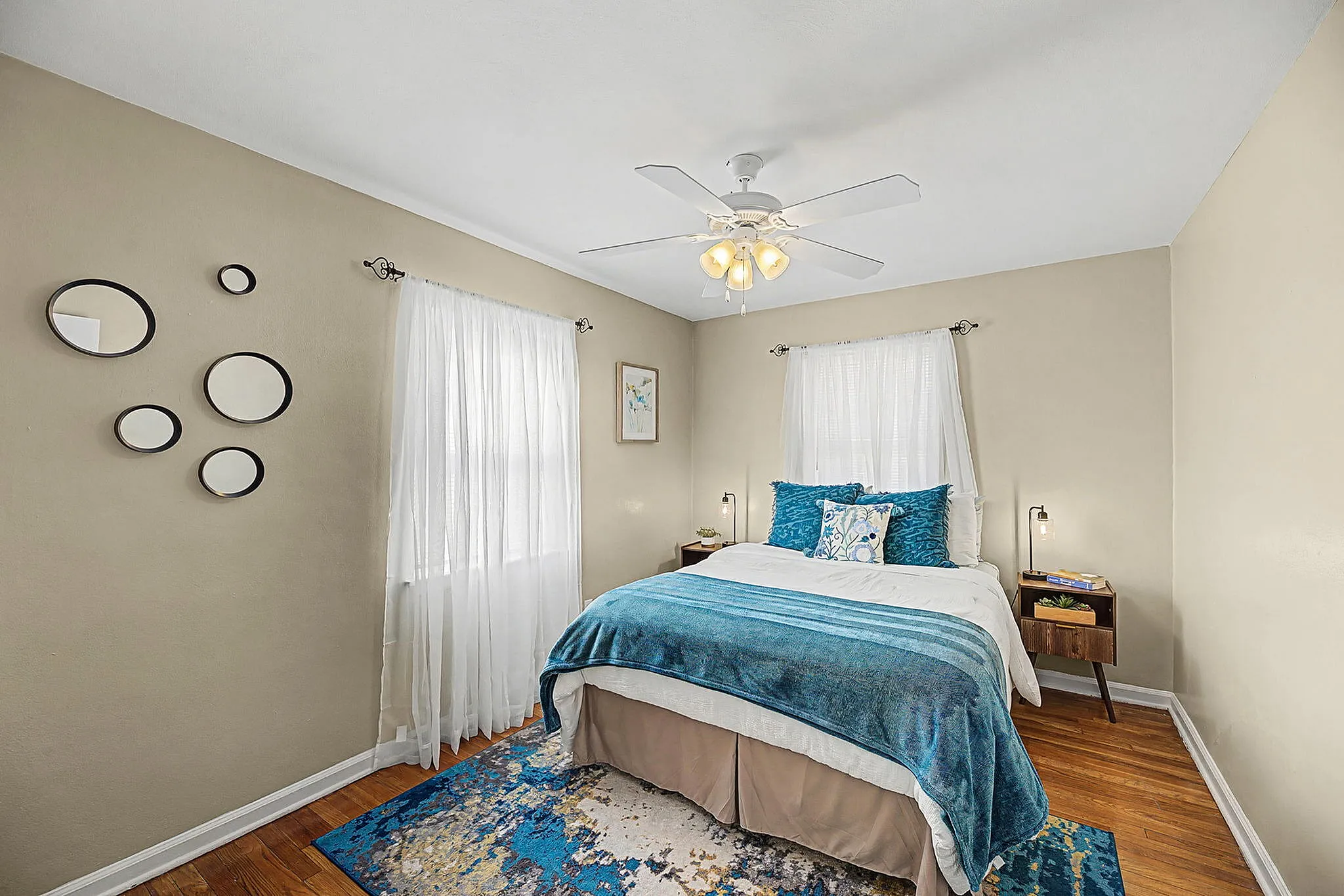 Charming bedroom with vibrant blue accents, hardwood floors, and elegant wall mirrors, creating a cozy and inviting atmosphere.