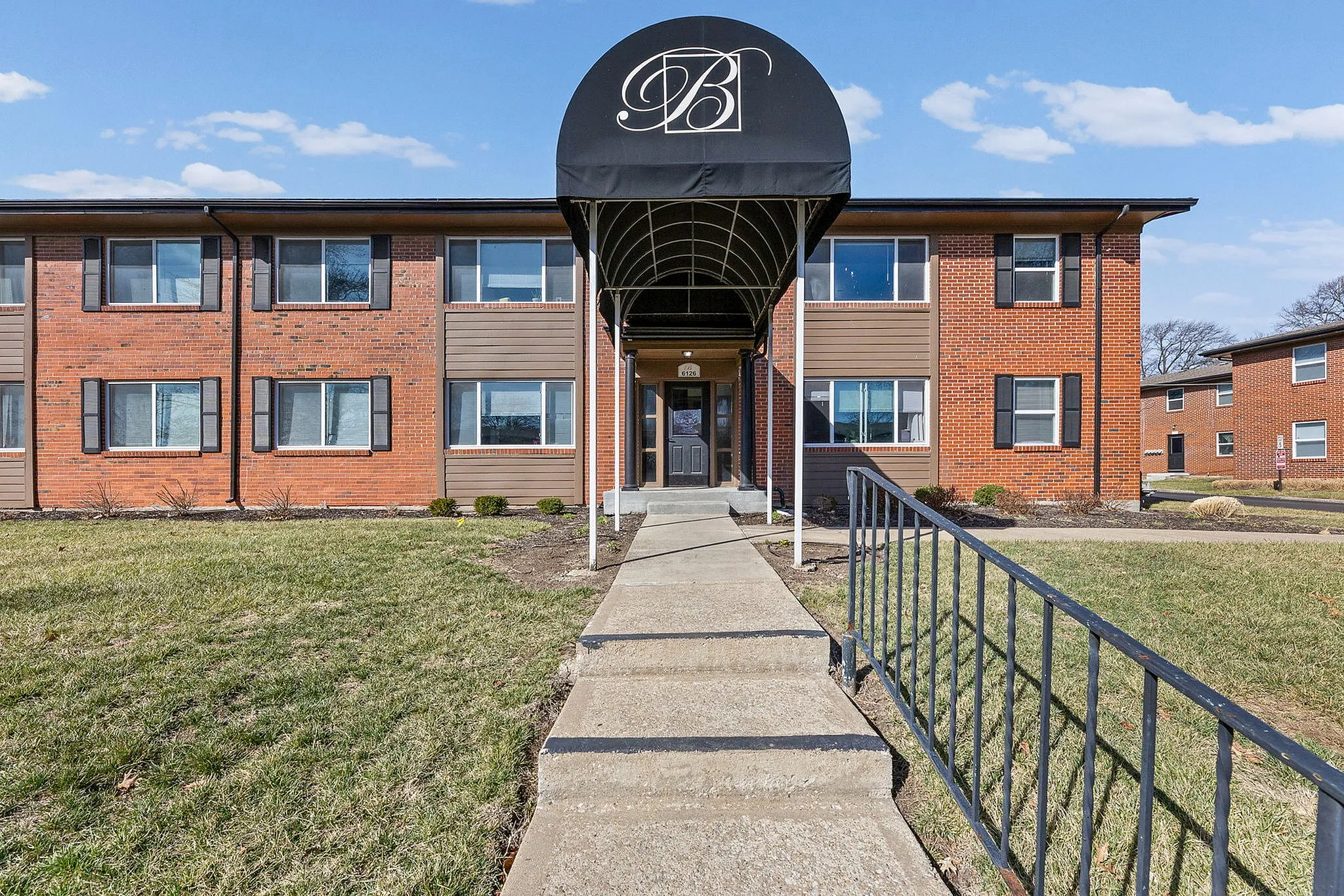 Charming brick apartment complex with modern awning and welcoming entrance, surrounded by manicured lawns.