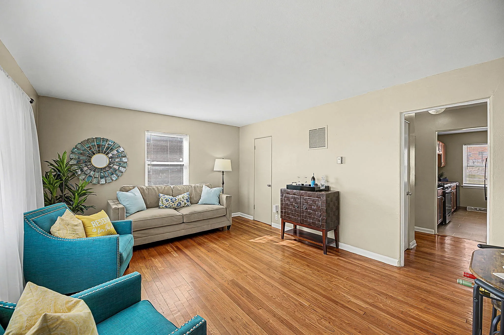 Bright and cozy living room with hardwood floors, accented by vibrant teal chairs and a stylish wall mirror, offering a welcoming ambiance.
