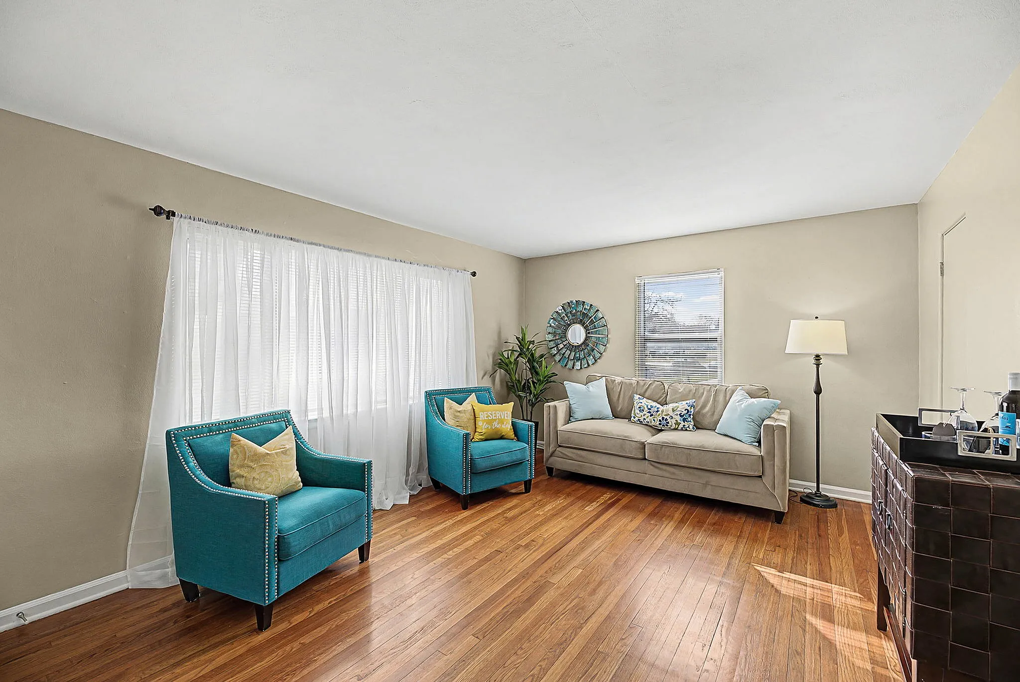 Bright and inviting living room featuring modern decor, plush beige sofa, two vibrant teal armchairs, and elegant wooden flooring.