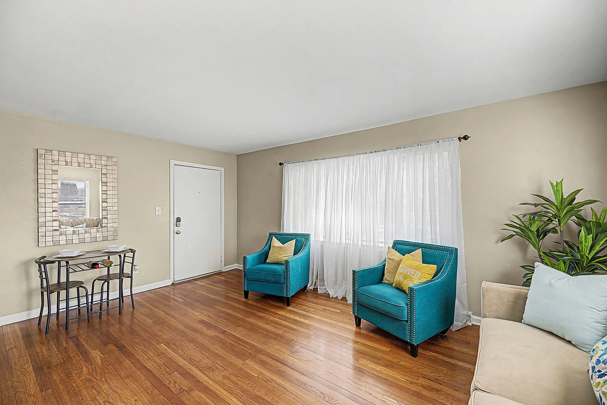 Bright and inviting living room with stylish teal armchairs, cozy pillows, elegant wooden floors, and a lush plant accenting the space.