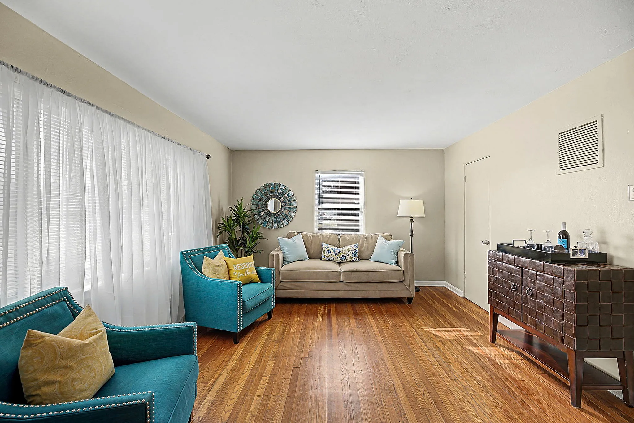 Inviting living room with vibrant teal armchairs, plush beige sofa, and stylish decor, creating a cozy and elegant atmosphere.