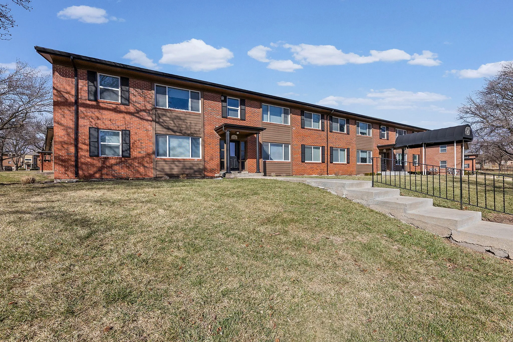 Charming two-story brick apartment building with large windows, surrounded by lush green grass and open sky.
