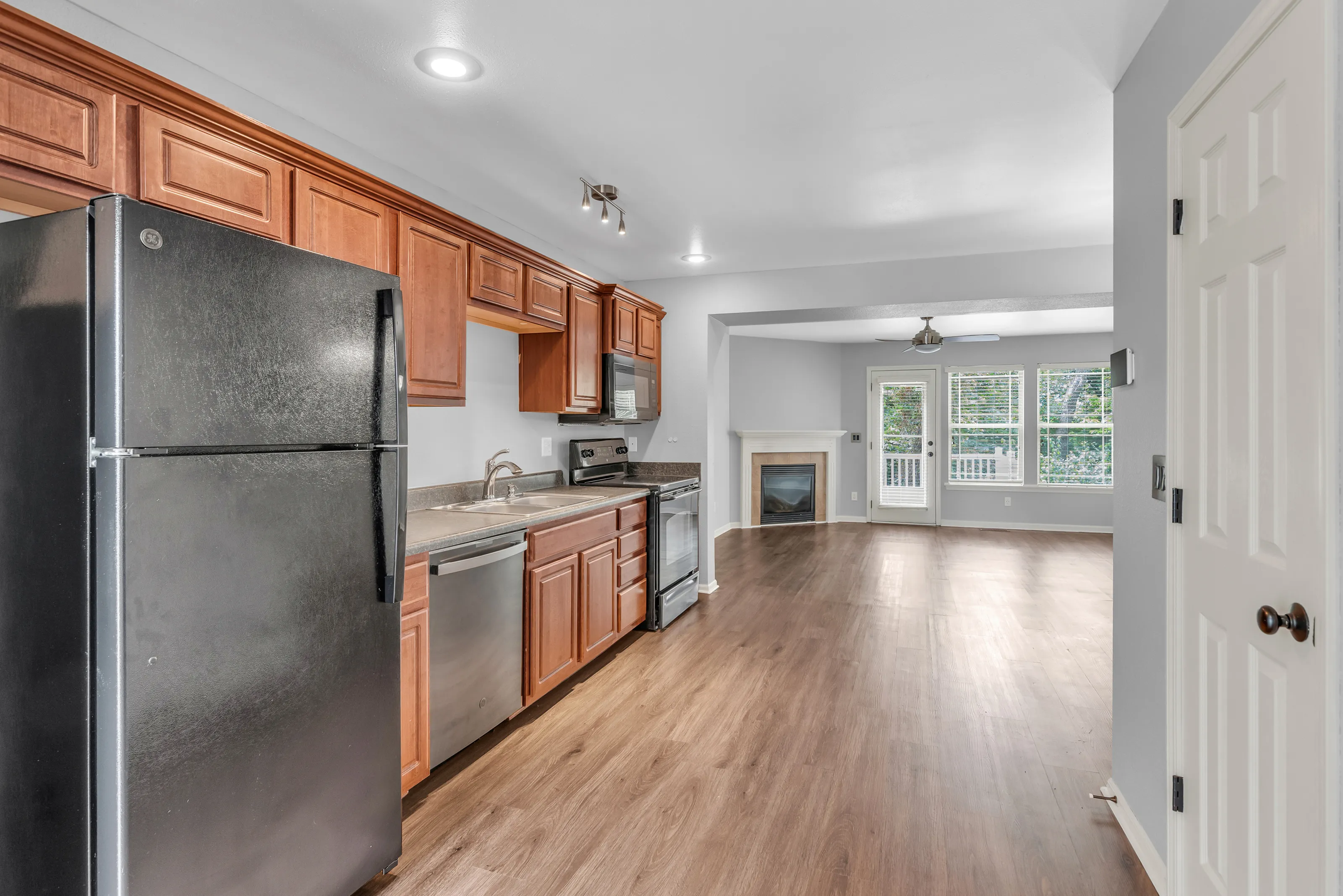 Modern open-concept kitchen with sleek wooden cabinets, stainless steel appliances, and bright, spacious living area featuring large windows and a cozy fireplace.