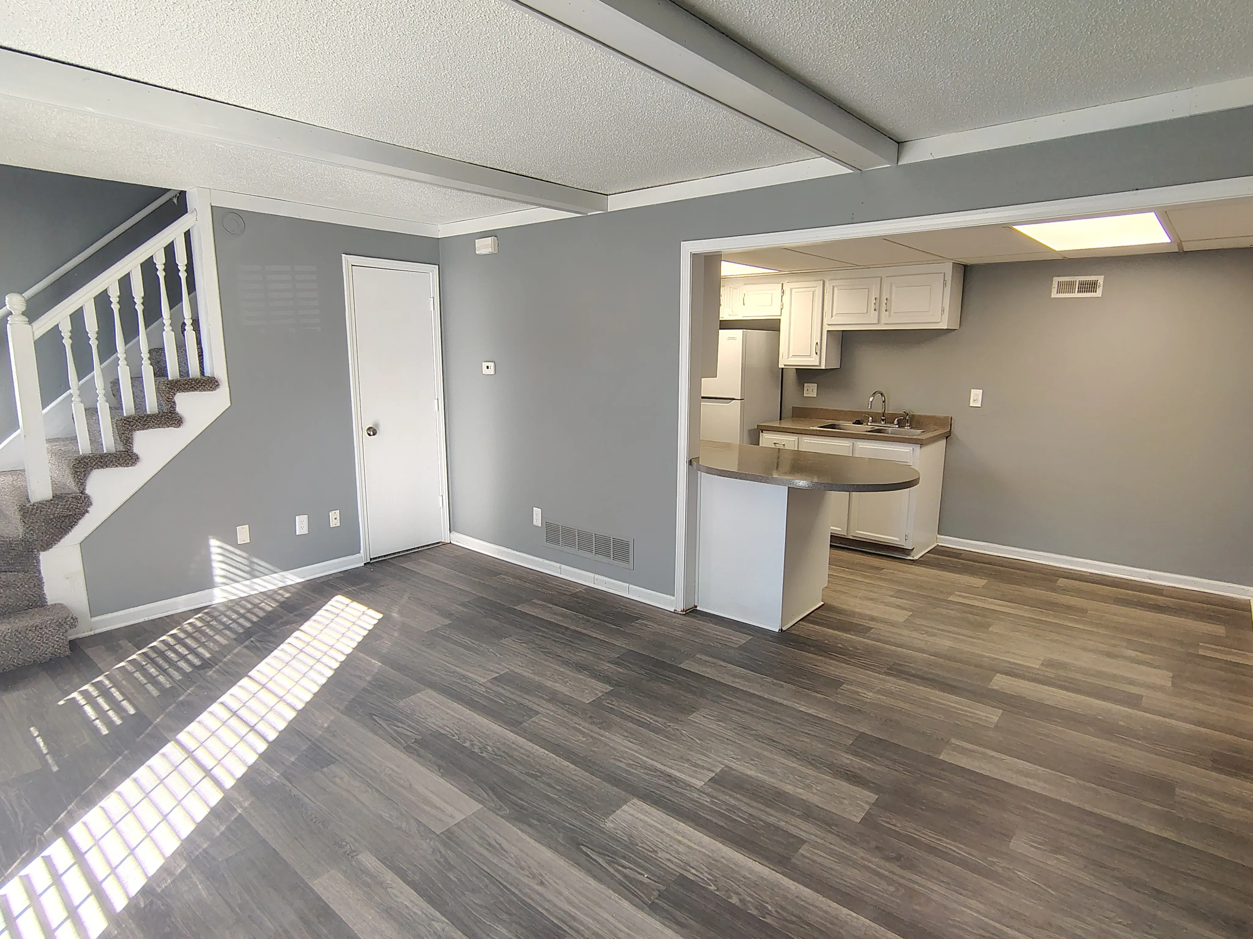 Modern open-plan living area with stylish laminate flooring, adjacent to a compact kitchen and elegant staircase.