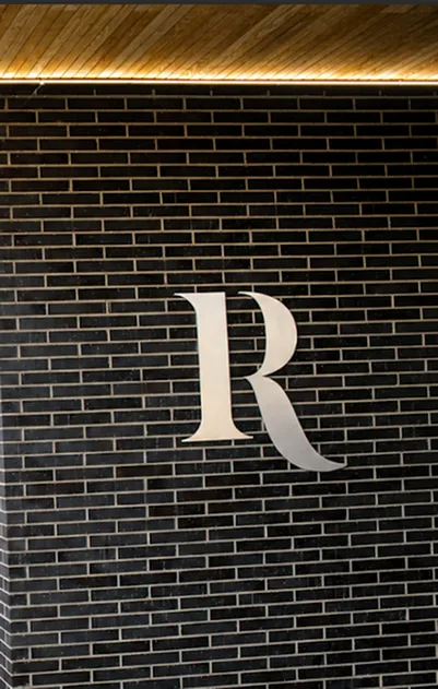 Elegant entrance featuring a sleek black brick wall with a prominent metallic letter \'R\', exuding modern sophistication.